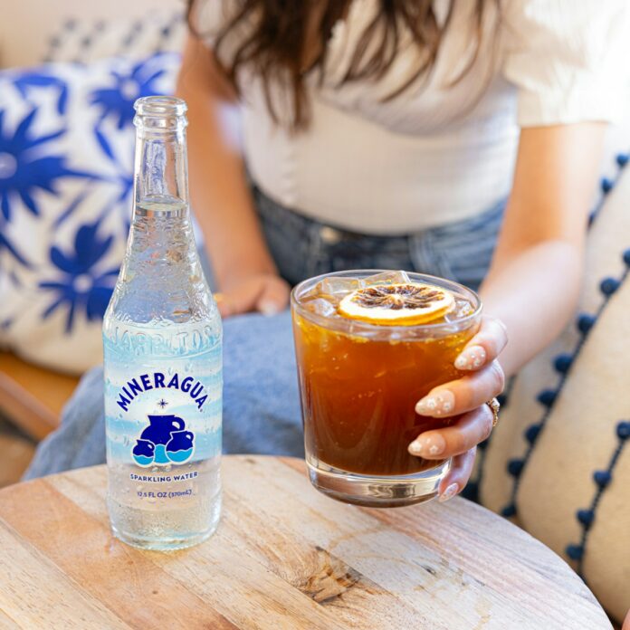 Photo by Mineragua Sparkling Water a woman sitting on a couch holding a glass of soda