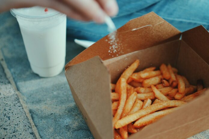 Photo by Emmy Smith person sprinkling salt in fries