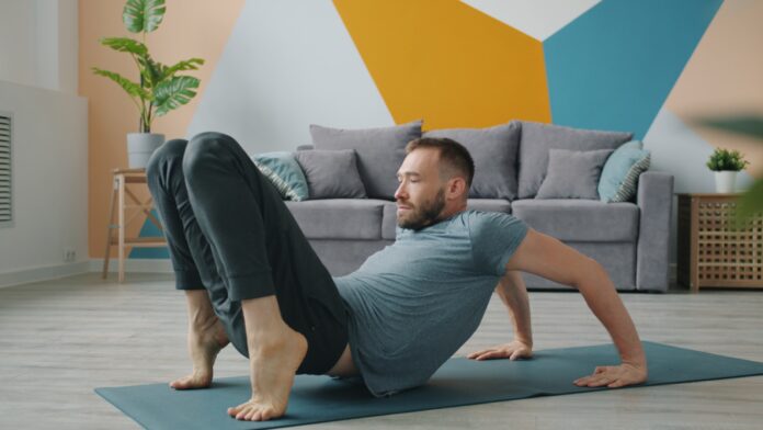 Photo by Vitaly Gariev Man doing yoga on a mat in a living room.